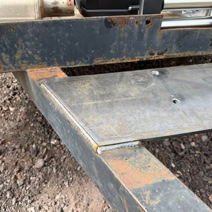 Rusty metal frame with silver surface and visible welds on construction site backdrop.