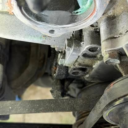 Close-up of a car engine showing oil leak near the gasket and damaged components.