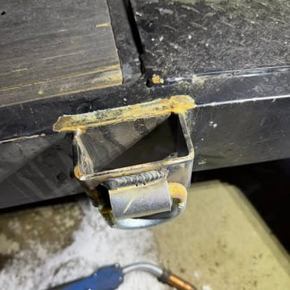 Close-up of a metal hitch receiver with visible rust and wear on a textured surface.