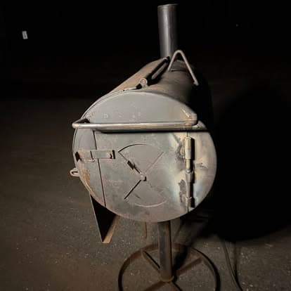 Vintage outdoor smoker with a cylindrical design, metal construction, and rusted finish.