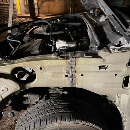Close-up of a car with an open hood showing engine components and a damaged chassis.
