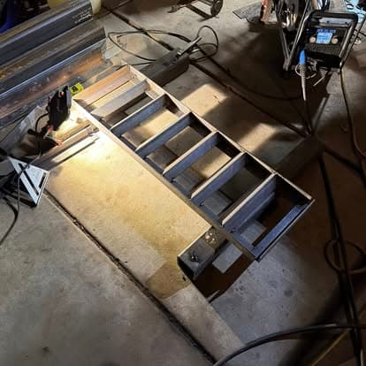 Metal fabrication workshop with a partially assembled ladder structure and tools visible.