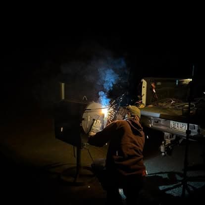 Welder working at night, producing sparks and smoke near a truck.