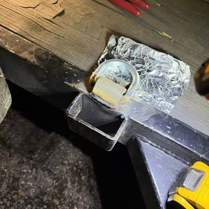 Close-up of a trailer hitch with metal latch and tools on a wooden surface at night.