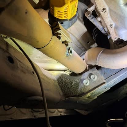 Under-car view of exhaust piping with a tool, highlighting maintenance work.