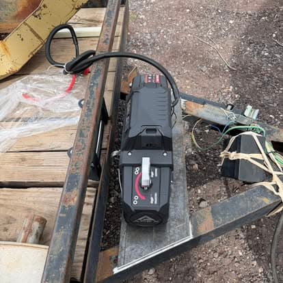 Portable winch mounted on a trailer with tools and cables in a gravel environment.