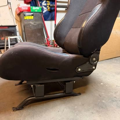 Racing seat with adjustable base in garage setting, showcasing fabric and metal construction.