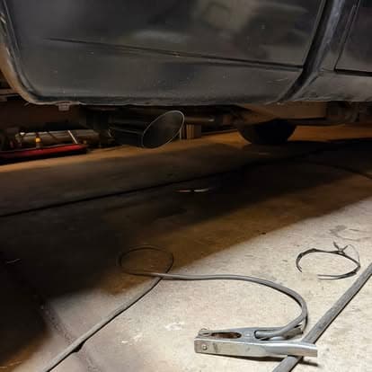Car exhaust system with a visible tailpipe and tools on a garage floor.