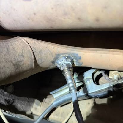 Close-up of a welded exhaust pipe showing a metal connector and wiring in a vehicle.