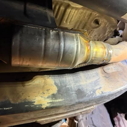 Close-up of an exhaust system with a metal pipe and welding details under a vehicle.