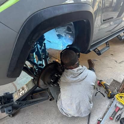 Mechanic welding under a vehicle, showcasing automotive repair and maintenance.